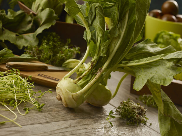 Kohlarbi turnip surrounded by leafy vegetables and microgreens on a wooden table