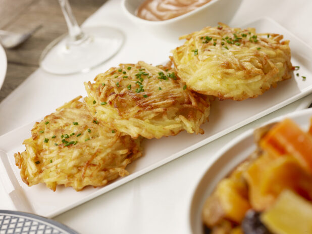 Three fried potato latkes on a white plate topped with fresh chiveson a white table cloth