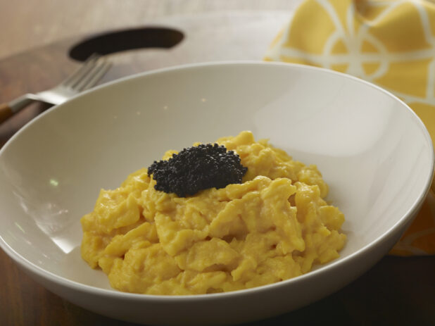 Large white bowl of soft scrambled eggs with black caviar on top