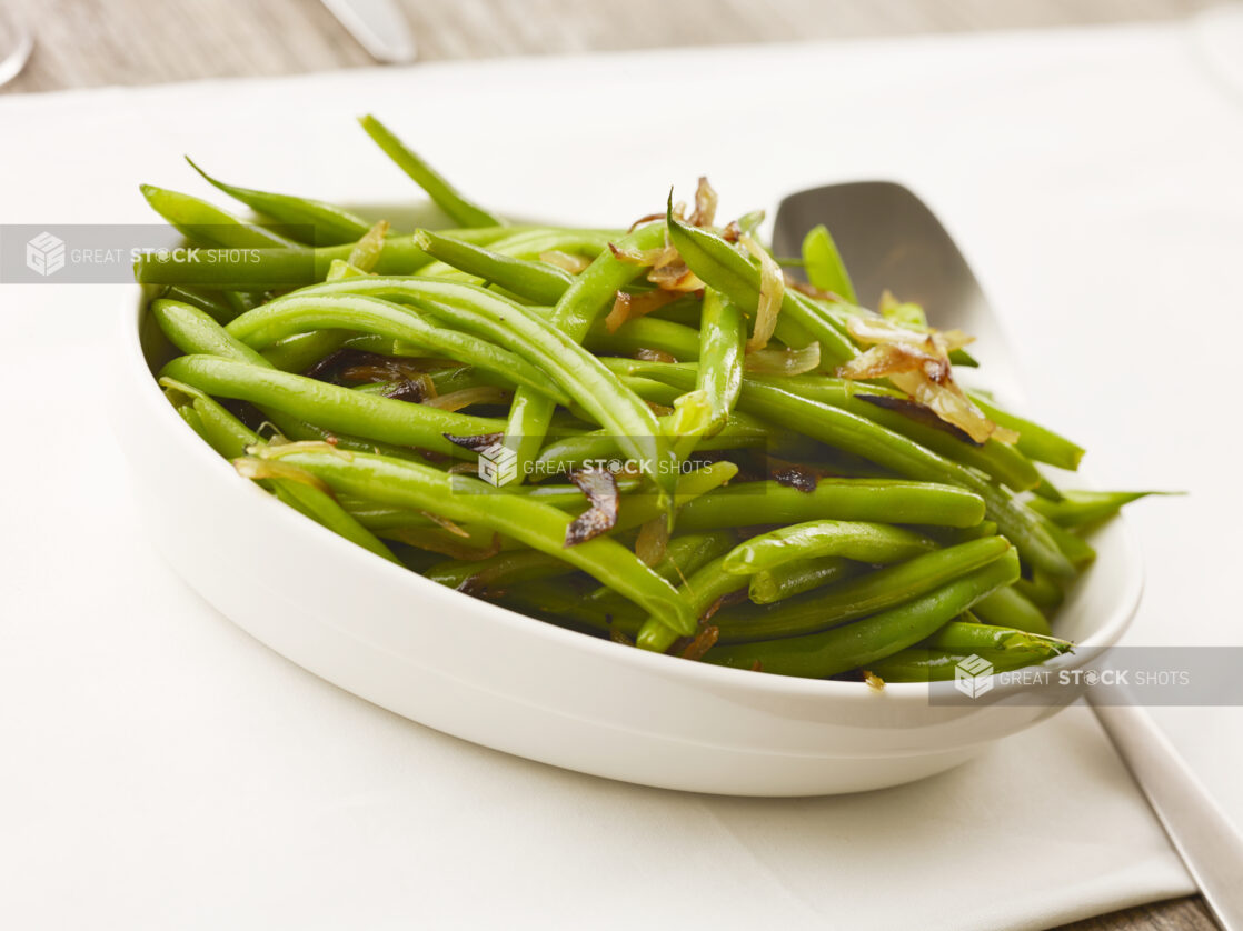 Bowl of cooked green beans with caramelized onions on a white table cloth