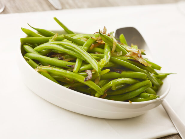 Bowl of cooked green beans with caramelized onions on a white table cloth