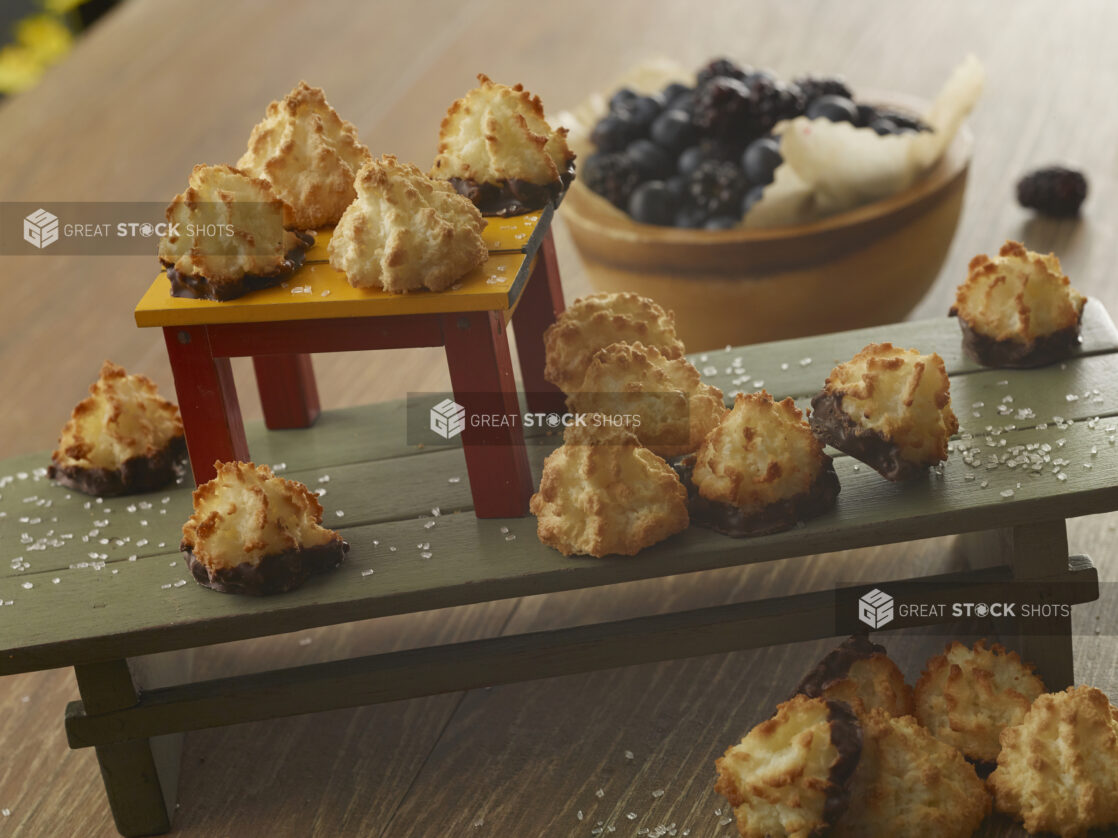 Two tiers of plain and chocolate dipped macaroons on wooden stands with a bowl of fresh berries in the background