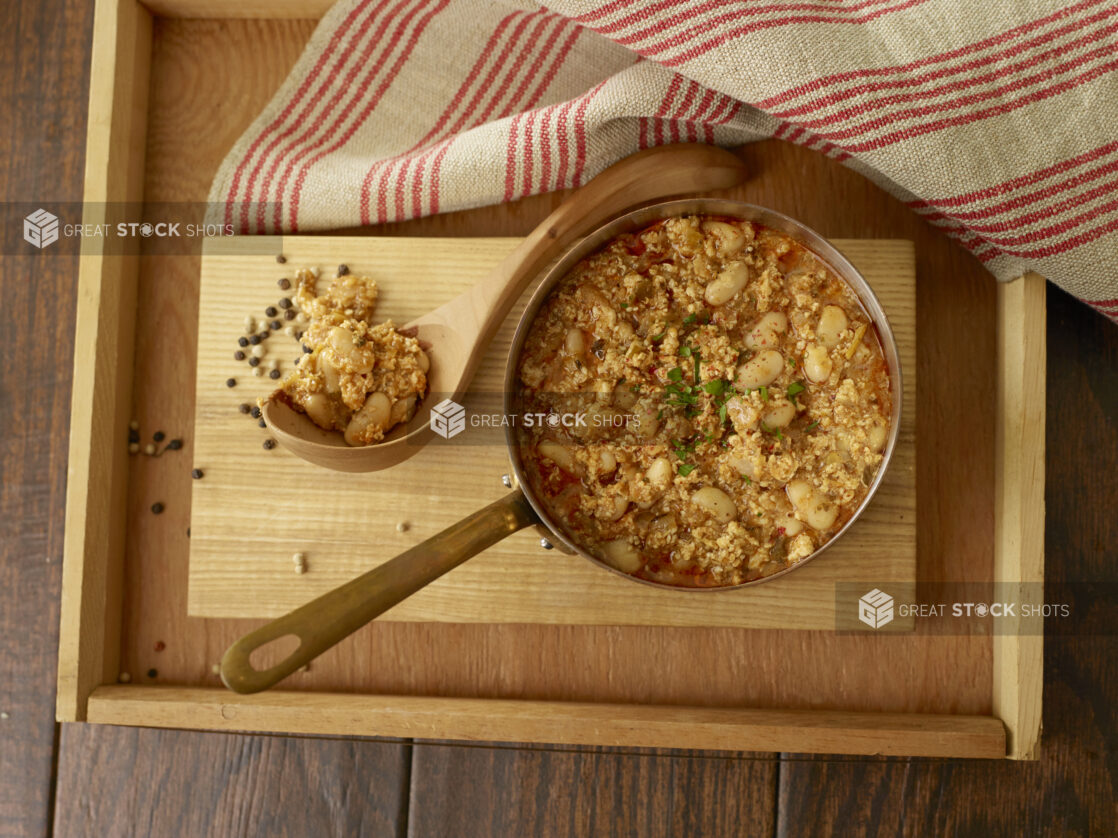 A pot of white bean and grains stew with ladle on a wood tray