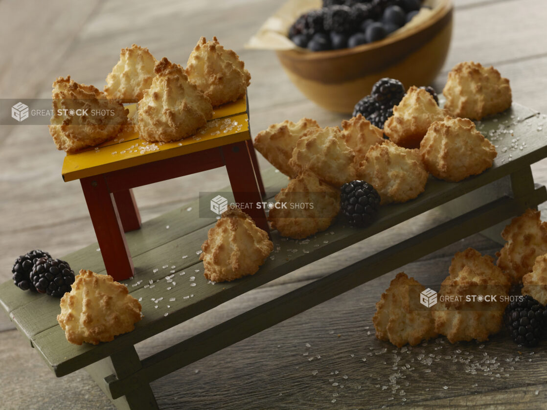 Two tiers of macaroons and blackberries on wooden stands with a bowl of fresh berries in the background