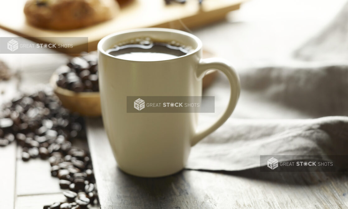 White ceramic mug filled with freshly brewed coffee with whole coffee beans in the background