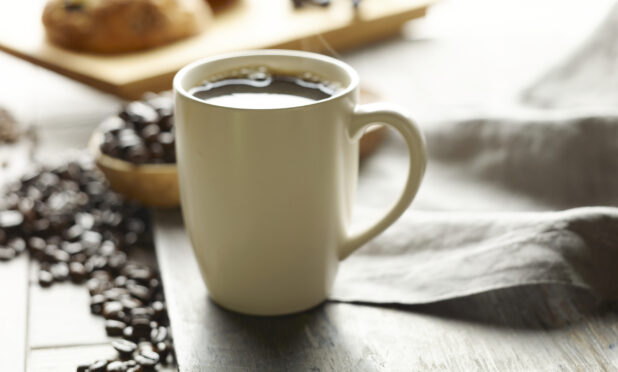 White ceramic mug filled with freshly brewed coffee with whole coffee beans in the background