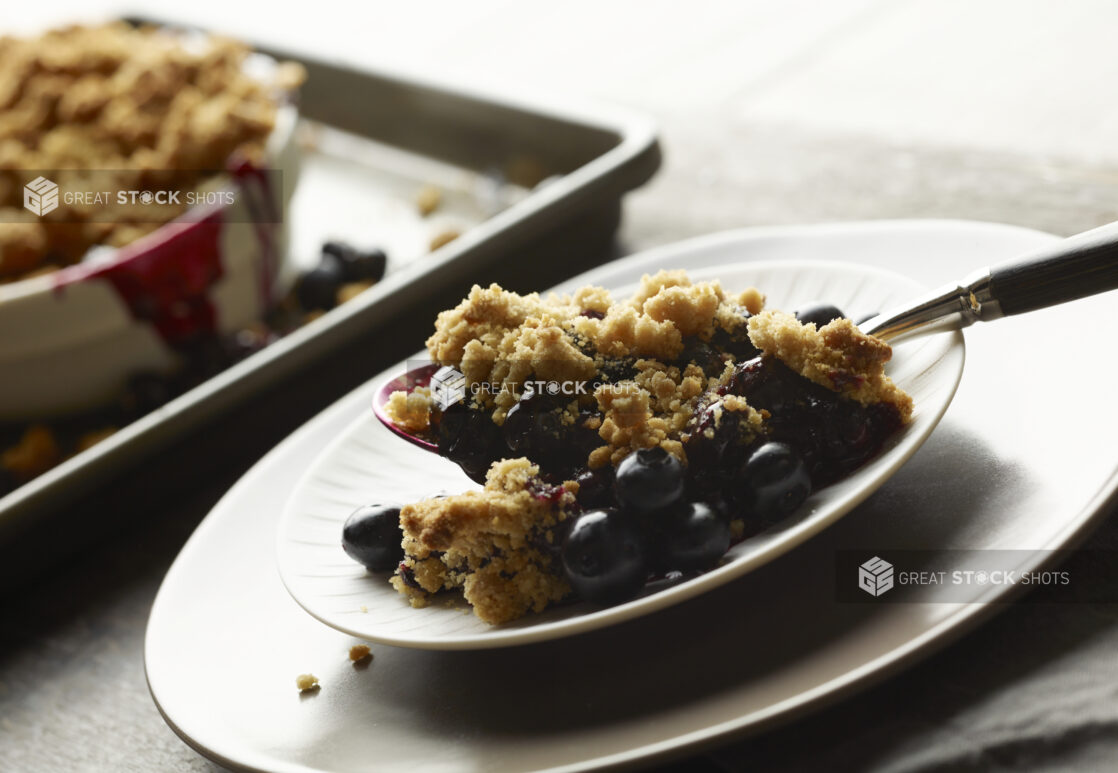 Small white bowl of blueberry crumble with a spoon