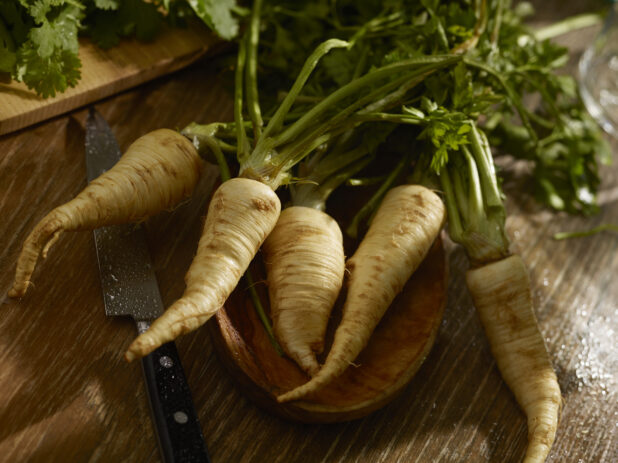 Fresh parsnips with stalk fresh from the garden on a wood table with a French knife