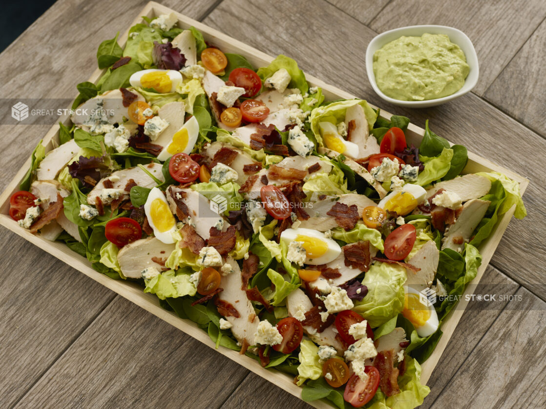 Overhead view of a cobb salad with green goddess dressing on the side on a wooden table