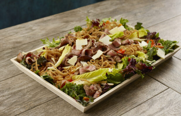 Large steak and fried onion salad with fresh parmesan and cherry tomatoes in a wood serving tray on a wood table