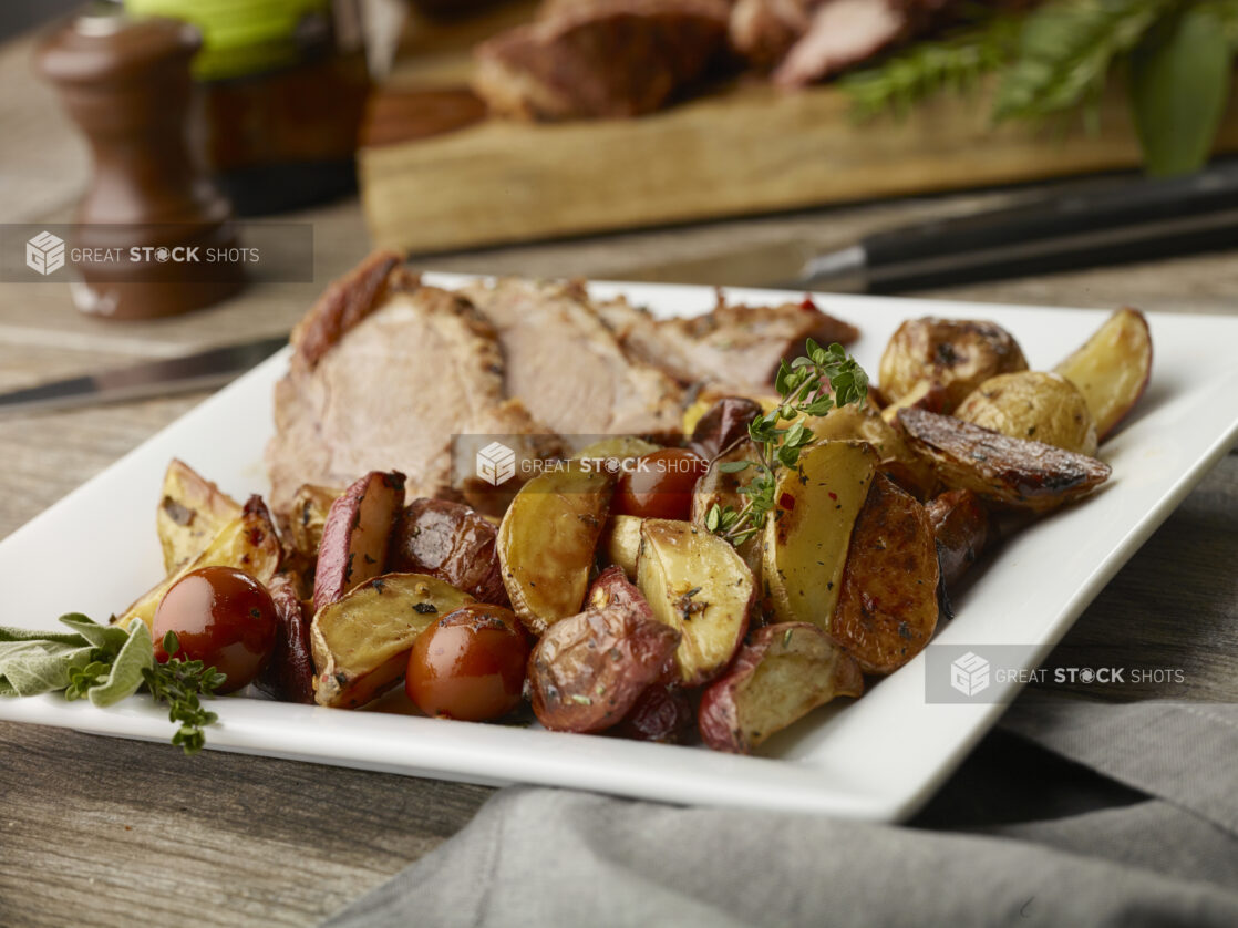 Main course of sliced prime rib roast with roasted potatoes and blistered cherry tomatoes on a white plate on a wood table