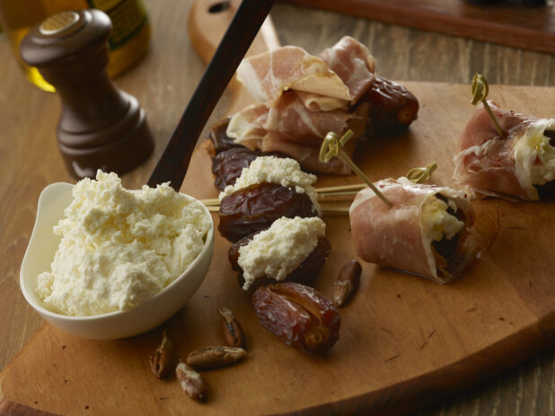 Making appetizers of goat cheese stuffed dates wrapped in prosciutto and pined with a bamboo toothpick on a wooden board