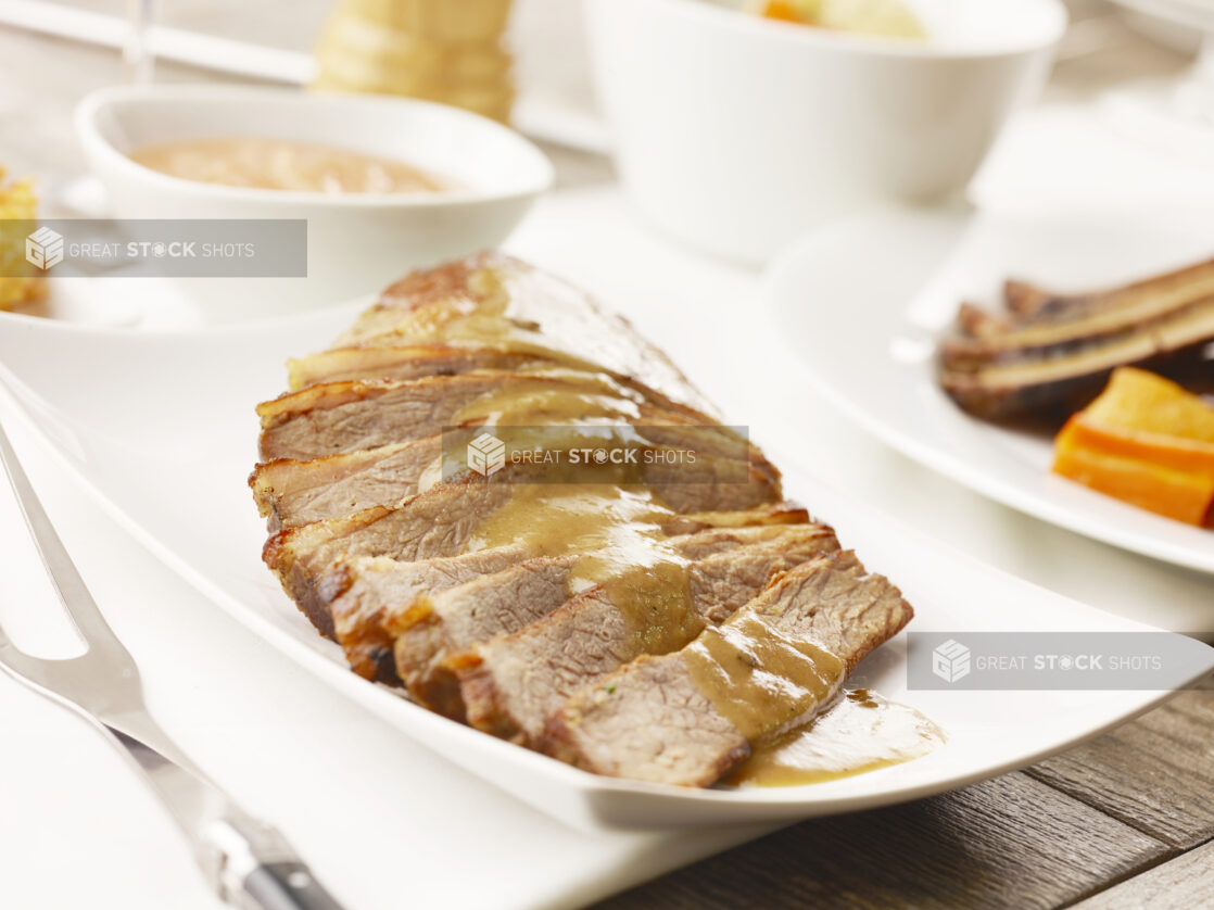 White plate of sliced beef brisket with gravy on top on a white table cloth