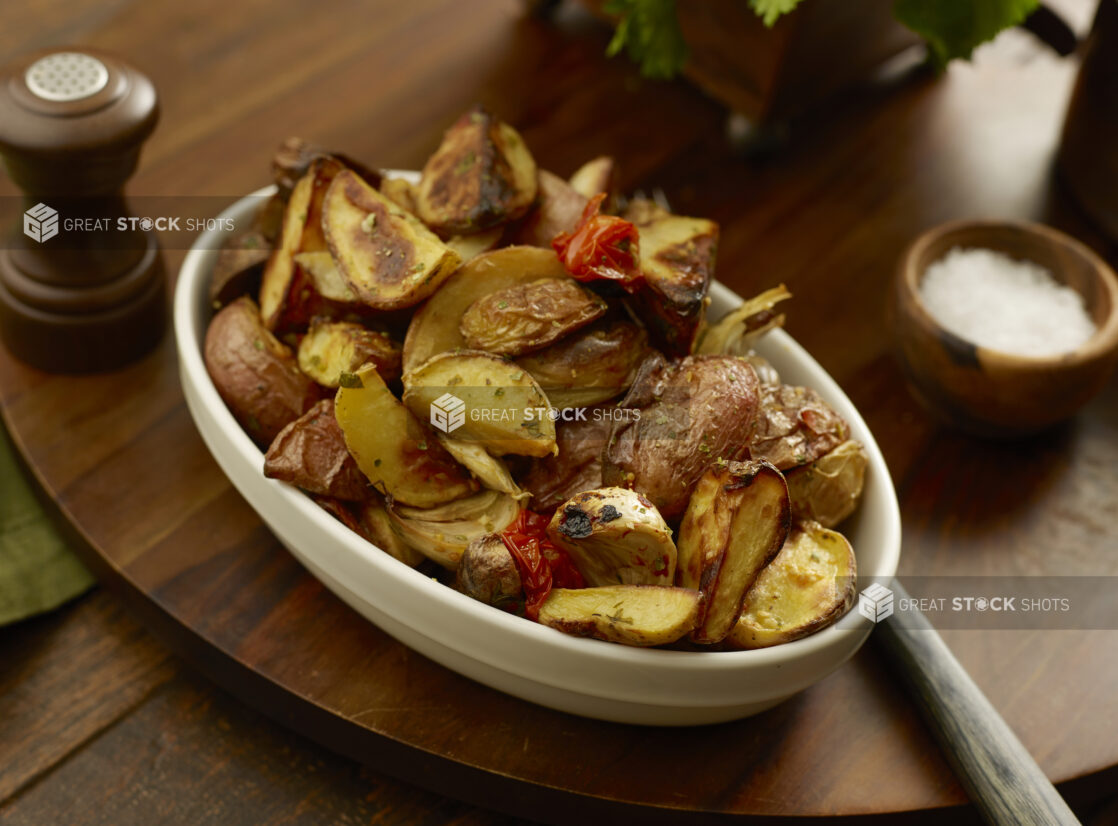 Bowl of roasted potato wedges, red peppers and garlic on a wooden board