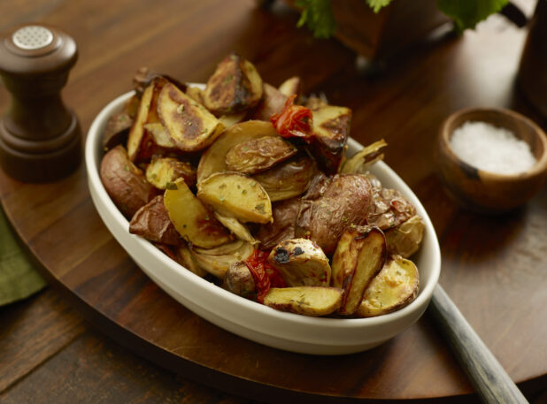 Bowl of roasted potato wedges, red peppers and garlic on a wooden board