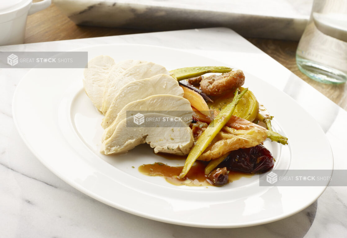 Plated dinner of sliced roast chicken with a side of root vegetables and prunes in a brown sauce on a marble slab