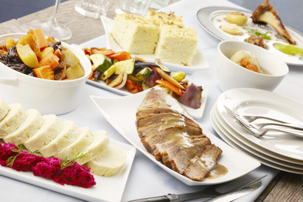 Selection of traditional Jewish dishes on a white table cloth on a wood table