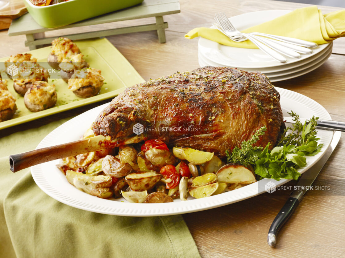 Large uncut bone in prime rib roast on a white serving platter with roasted potatoes and cherry tomatoes