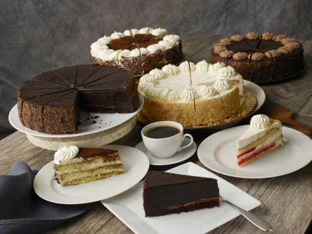 Assortment of cakes on stands and cake slices on plates with a napkin on a wood table