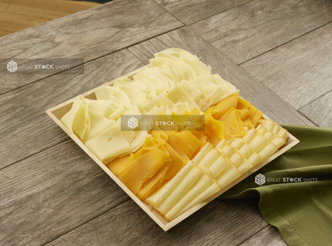 Four different types of cheese layered in columns on a wooden catering tray on a wood table with a napkin