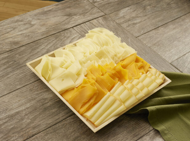 Four different types of cheese layered in columns on a wooden catering tray on a wood table with a napkin