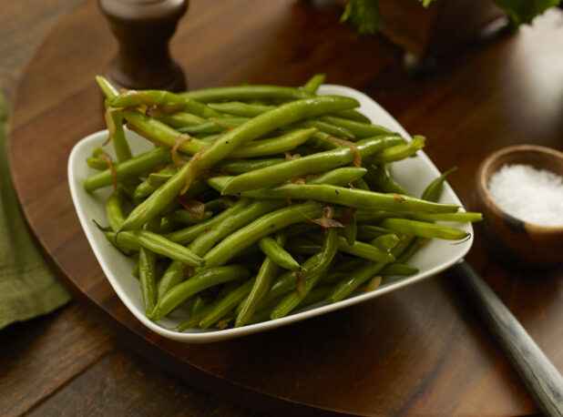 Bowl of cooked green beans with caramelized onions on a wooden board