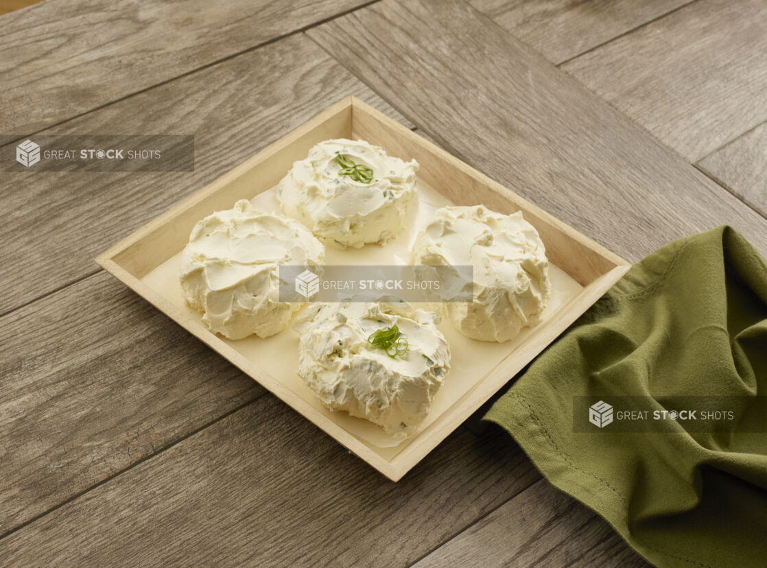 Two flavors of cream cheese in four balls on a wooden catering tray with parchment paper on a wood table