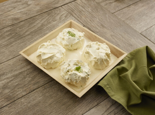Two flavors of cream cheese in four balls on a wooden catering tray with parchment paper on a wood table