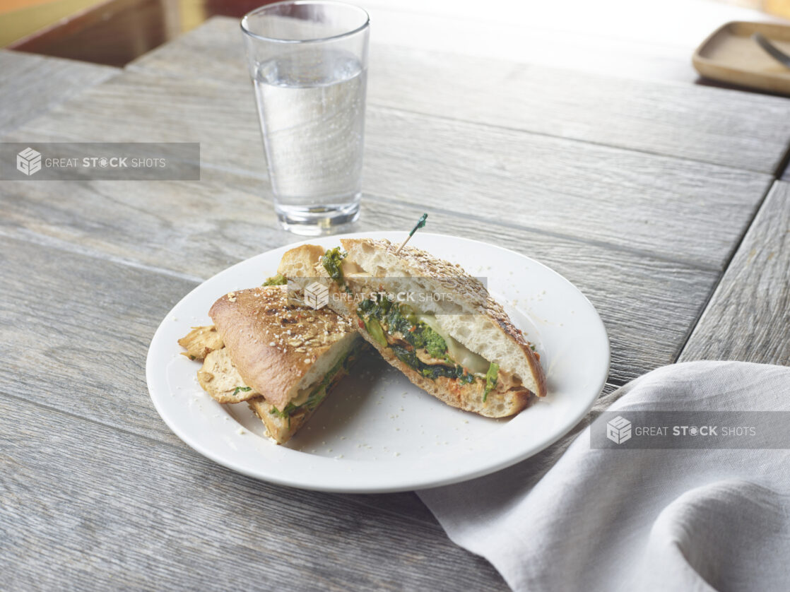 Grilled chicken panini sandwich with spinach, pesto, cheese and sauce on white plate topped with parmesan cheese and a toothpick on a wood table