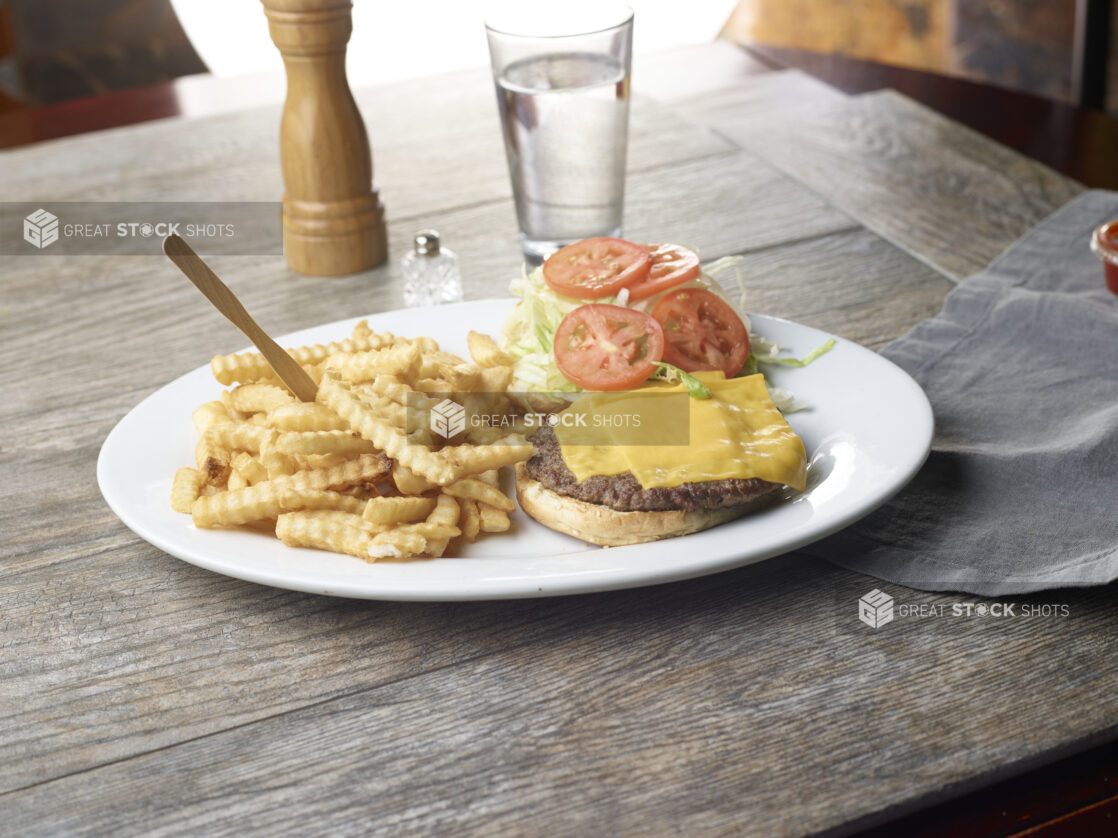 Plate with cheeseburger and a side of crinkly french fries on a wooden table