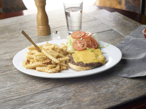 Plate with cheeseburger and a side of crinkly french fries on a wooden table