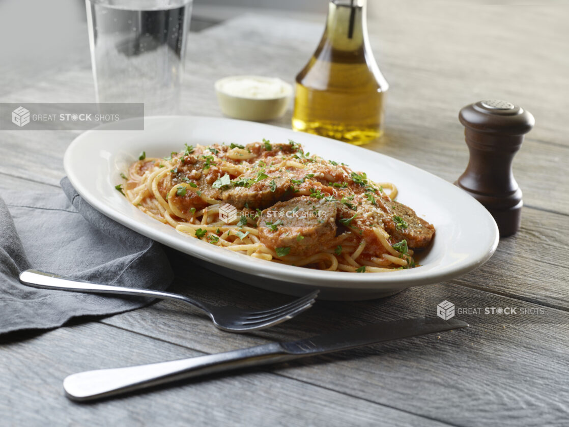 White plate of spaghetti and meatballs with grated parmesan and parsley on top