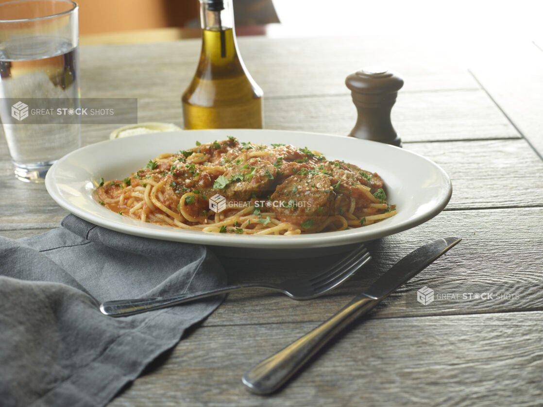 White plate of spaghetti and meatballs with grated parmesan and parsley on top