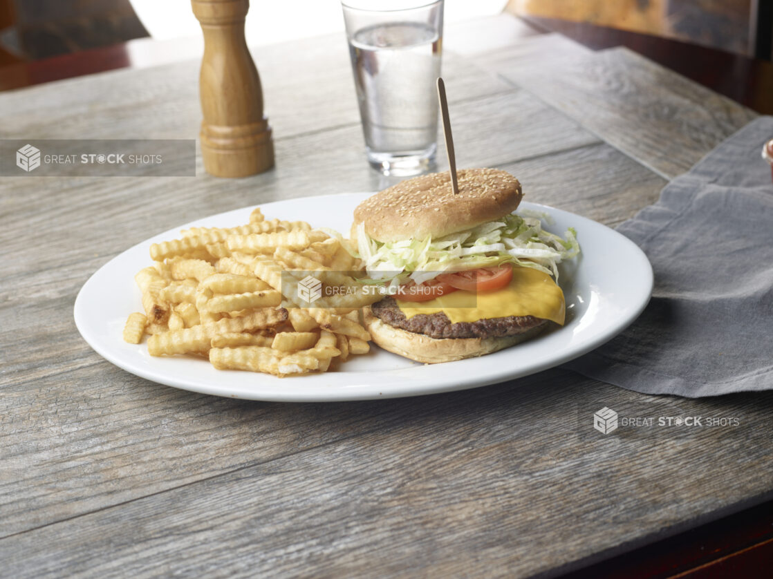 Plate with cheeseburger and a side of crinkly french fries on a wooden table