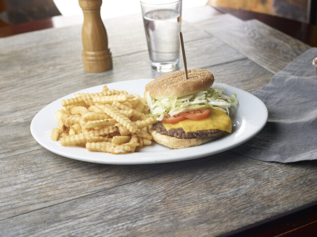 Plate with cheeseburger and a side of crinkly french fries on a wooden table