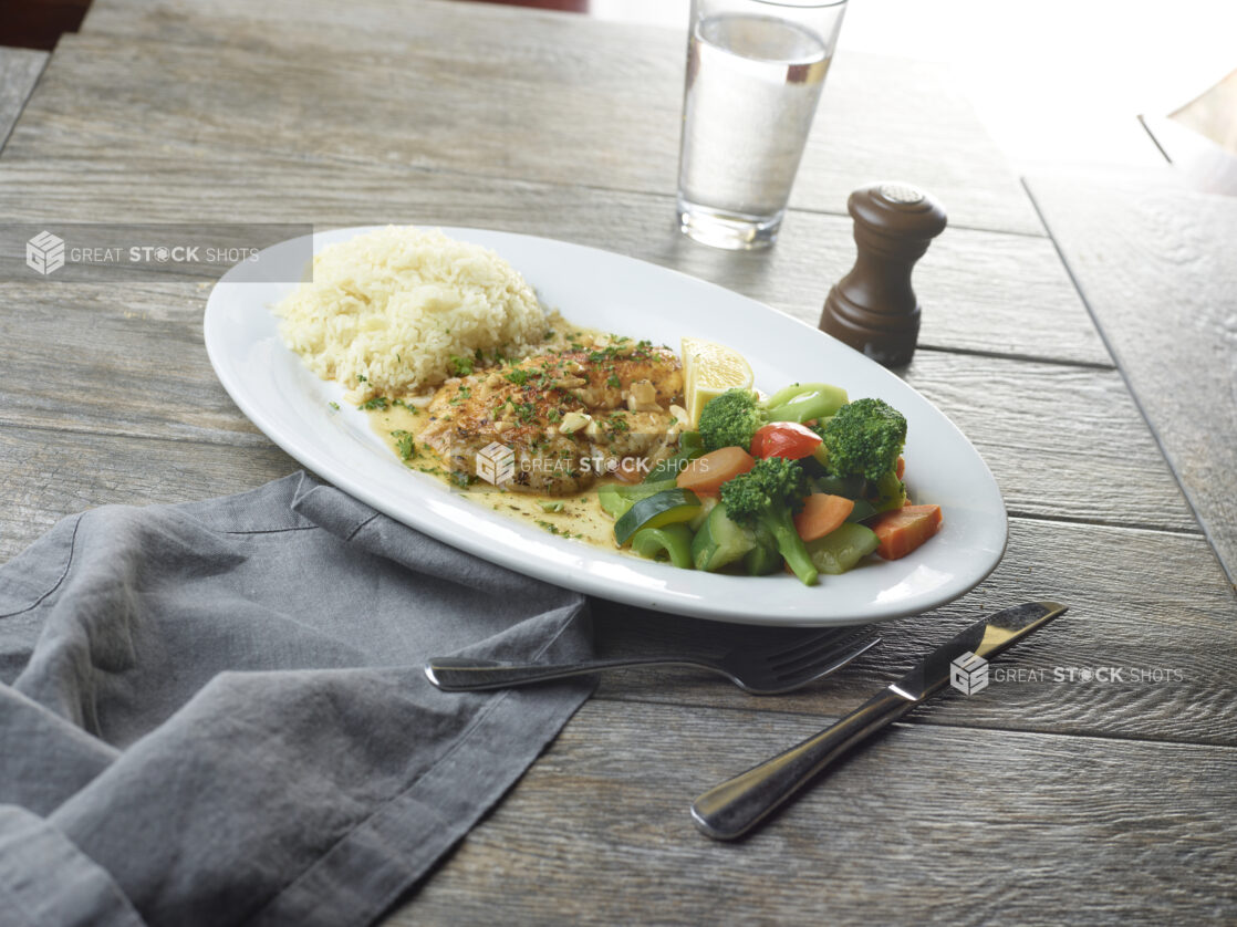 Plate of white pan-seared white fish in a lemon garlic sauce with steamed vegetables on a wooden table