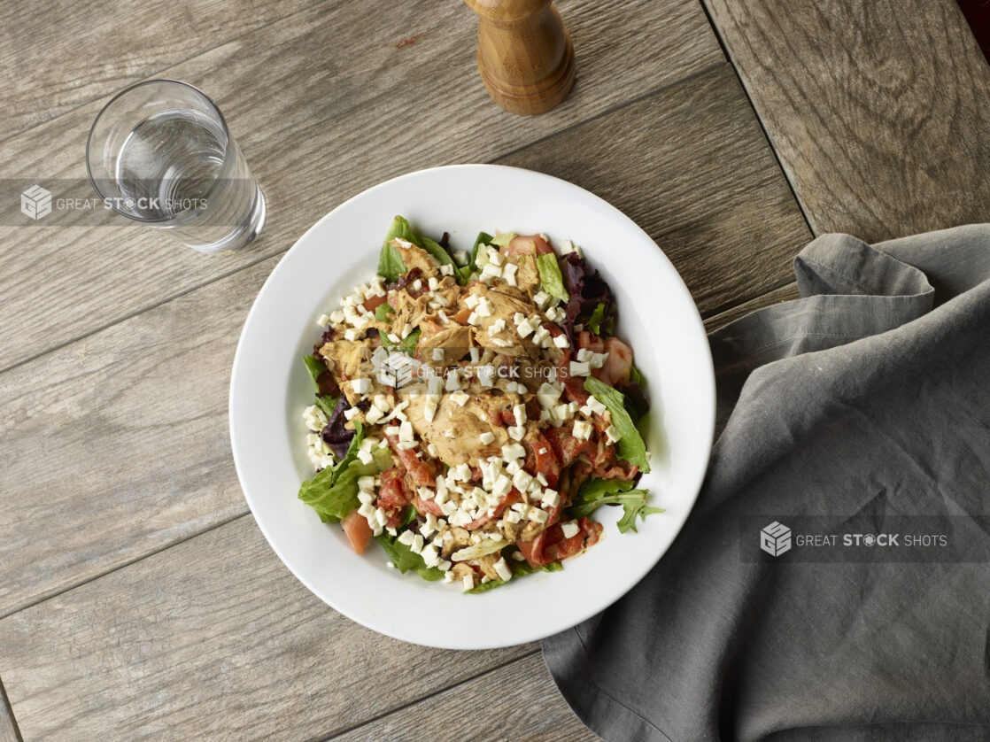 Salad of greens, chicken, and red peppers with feta topping on a white plate