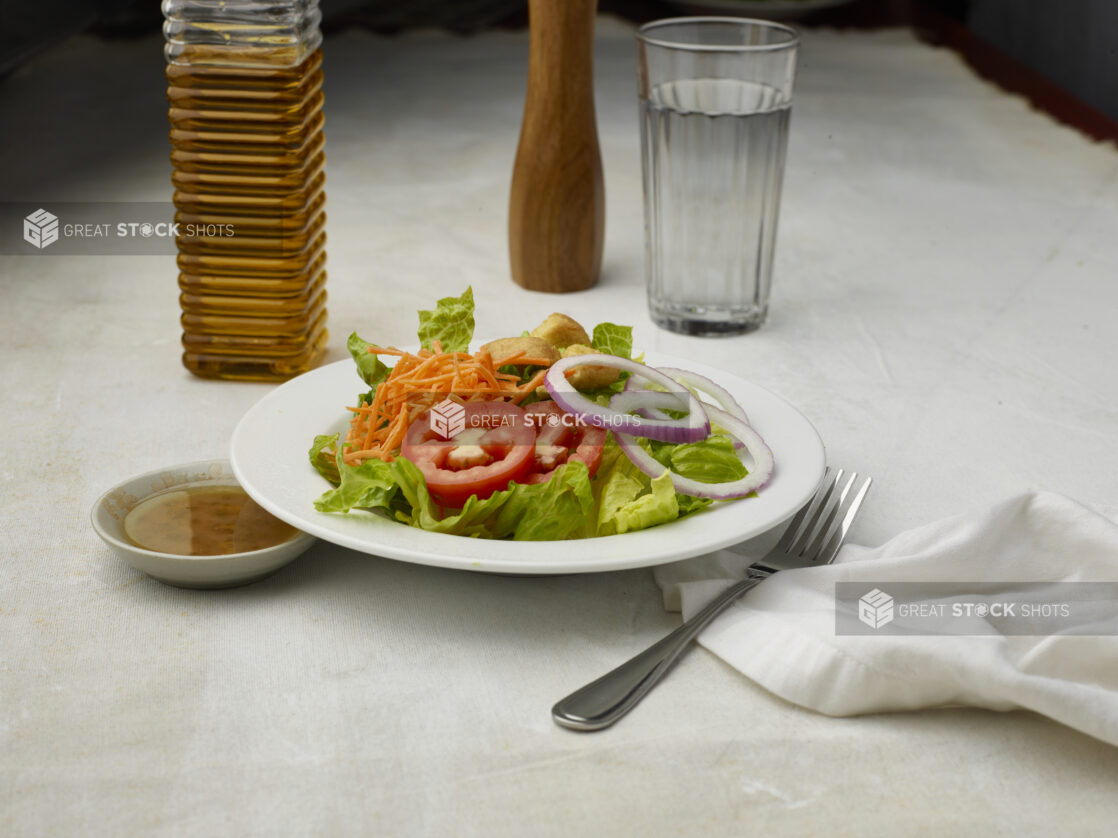 Garden salad with dressing on the side on a white table cloth with glass of water in the background