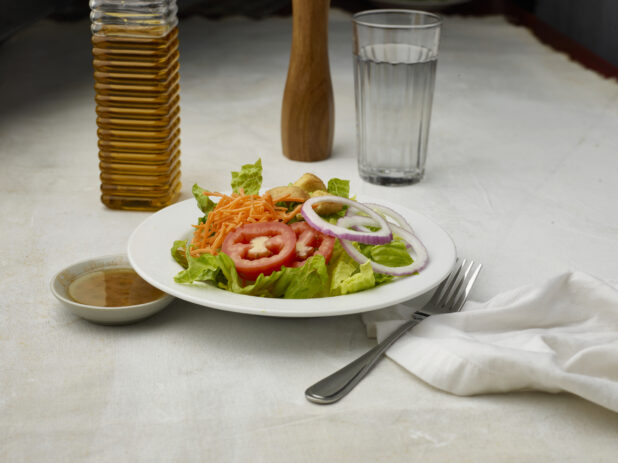 Garden salad with dressing on the side on a white table cloth with glass of water in the background