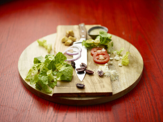 Chopped ingredients for a salad with a chefs knife on a wooden board on a red wooden table
