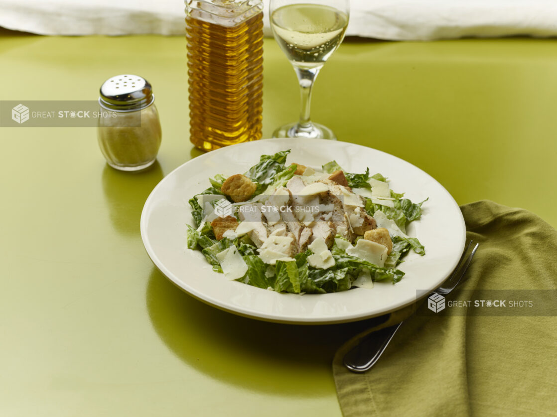 Chopped Caesar salad with a glass of white wine on a green background