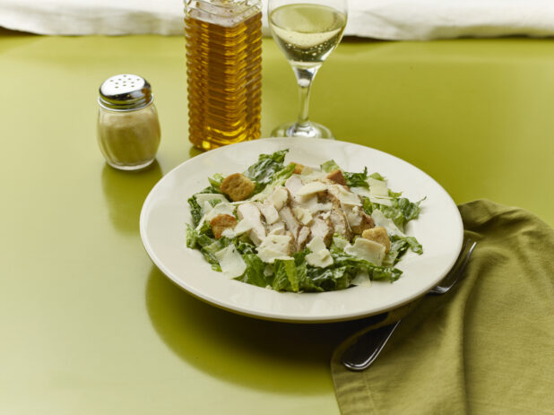 Chopped Caesar salad with a glass of white wine on a green background