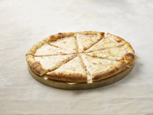 Sliced cheese pizza on a wooden board with parchment paper