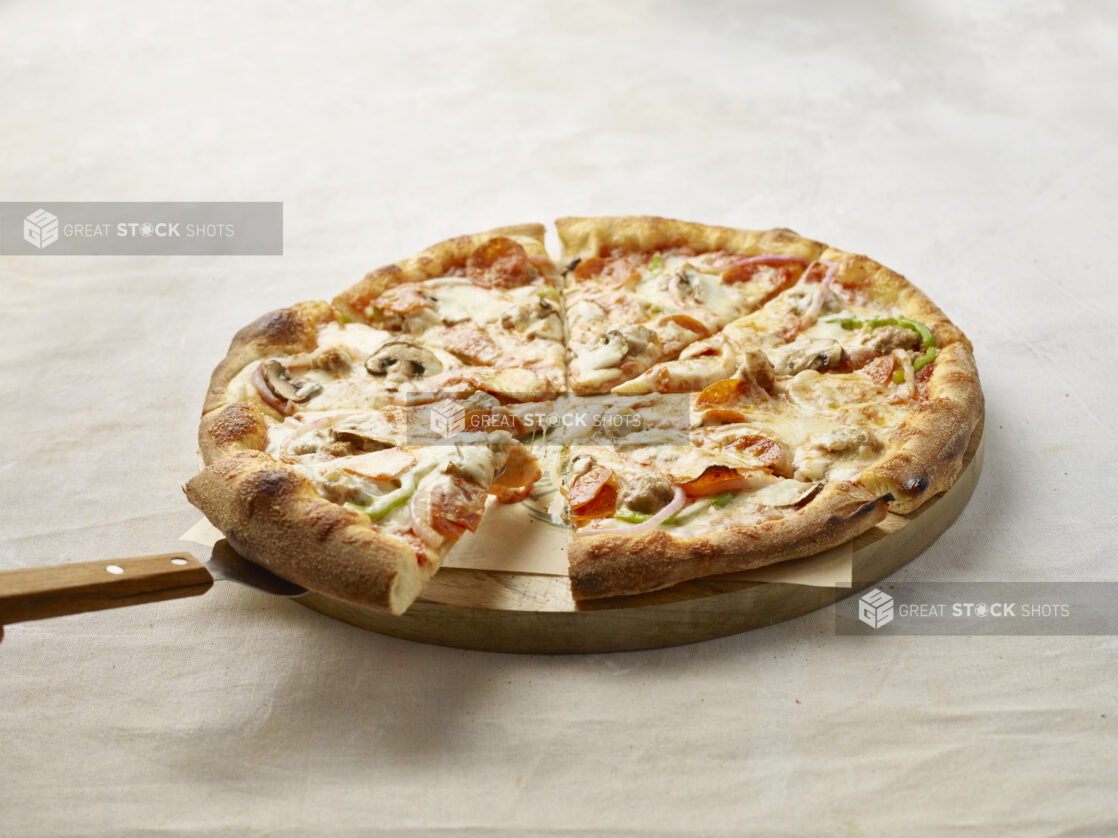 Hand lifting up a slice of Deluxe pizza on a wooden board with parchment paper