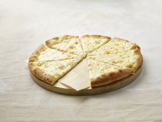 Sliced cheese only pizza with a slice missing on a wooden board with parchment paper