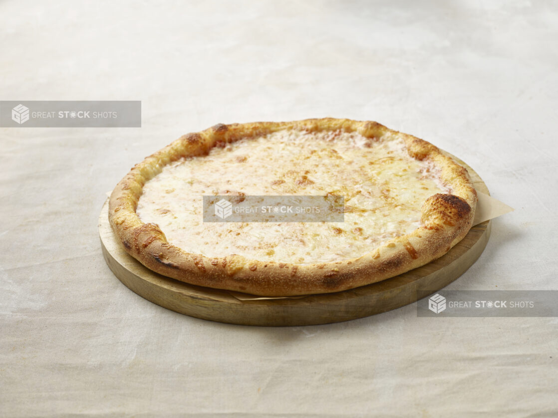 Whole cheese pizza on a wooden board with parchment paper