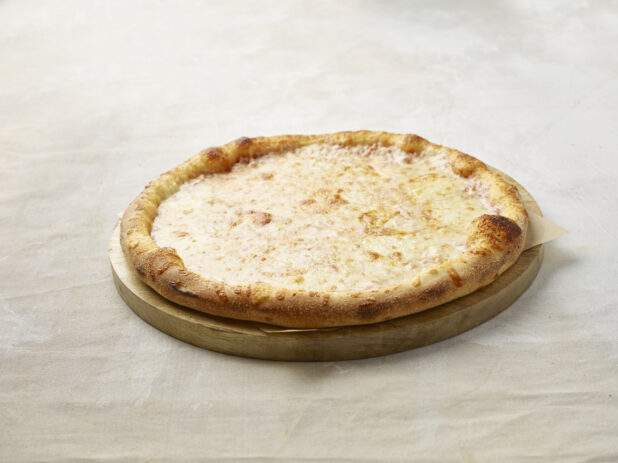 Whole cheese pizza on a wooden board with parchment paper