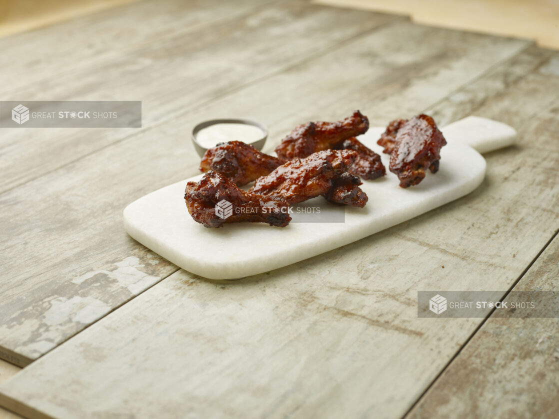 Sauced chicken wings on a marble board with a creamy dipping sauce on a wooden background