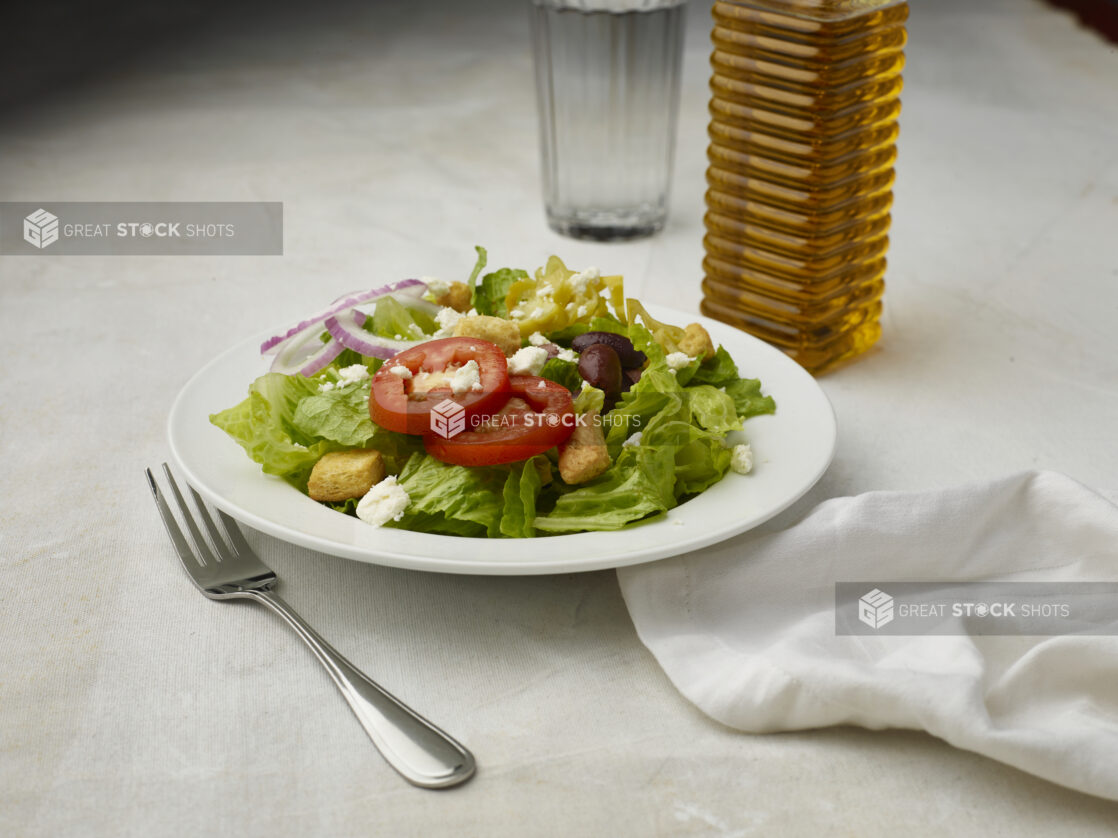 Greek salad with no dressing on a white table cloth with glass of water in the background