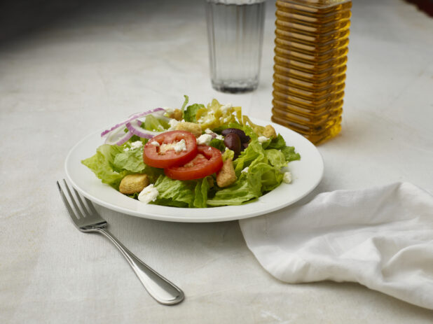 Greek salad with no dressing on a white table cloth with glass of water in the background